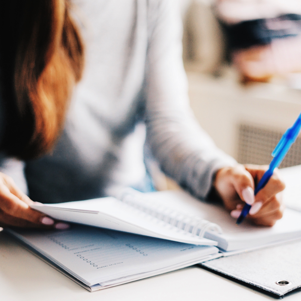 A closeup shot of a woman writing with a blue pen in a paper planner.