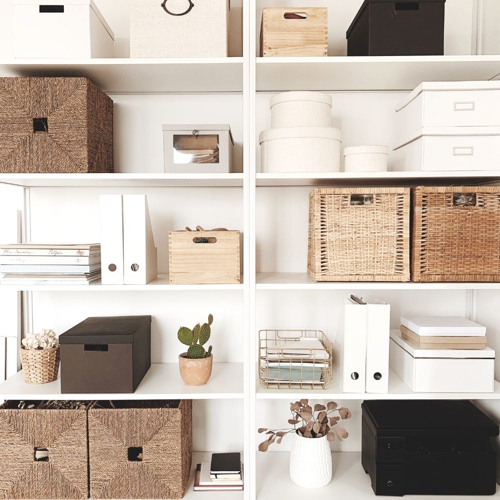 White shelves with boxes, baskets, containers, books, and plants all in a neutral color scheme.